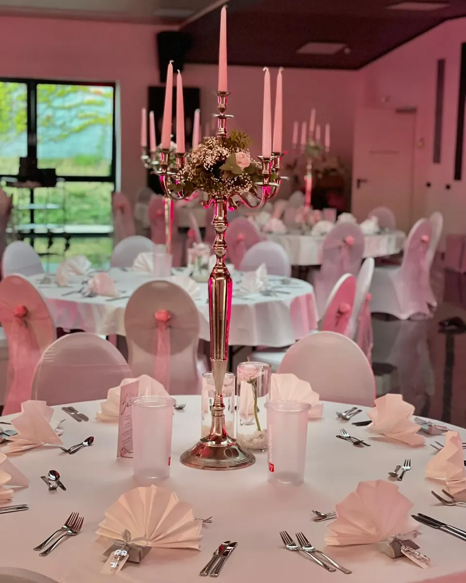 Hallenraum mit runden Tischen, Kandelabern und Stuhlschleifen in Rosa vor der Fensterfront
