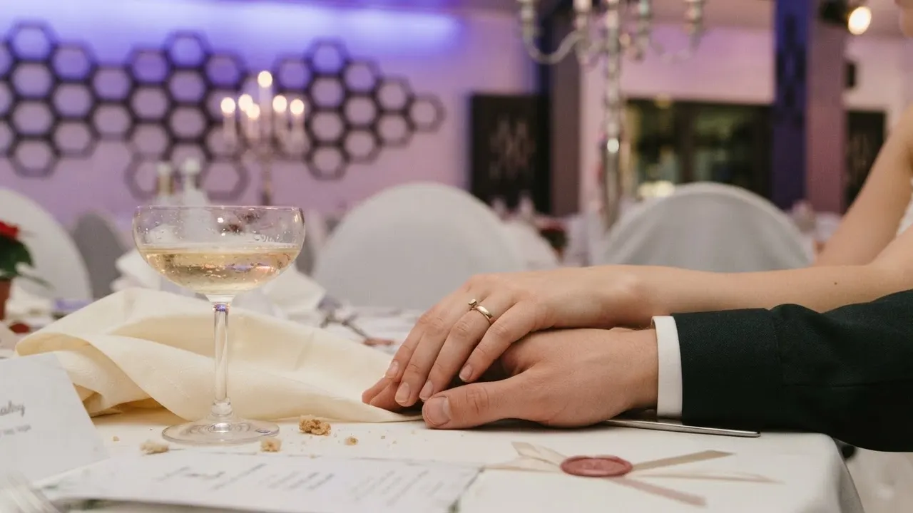 Zwei Hände mit Ring auf einem Tisch neben einem Champagnerglas und einer Menükarte mit Wachssiegel